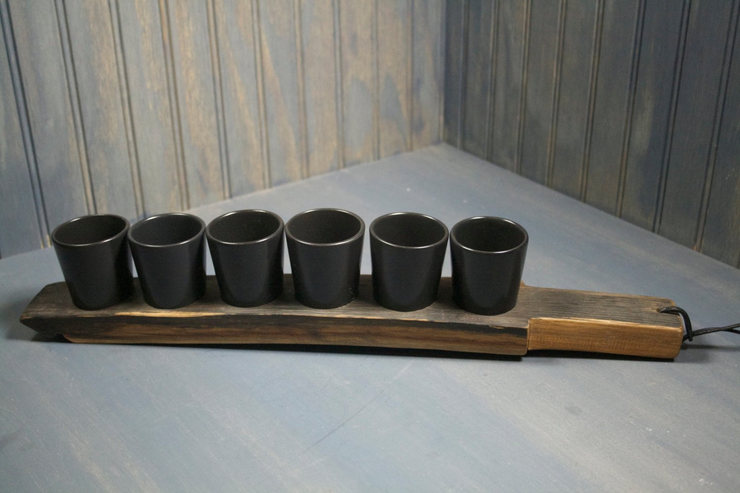 WHISKEY BARREL SHOT PADDLE WITH BLACK CERAMIC SHOT GLASSES - Black Ceramic shot glasses with a reclaimed whiskey barrel shot paddle and leather handle, 6 shot glasses/sake cups included