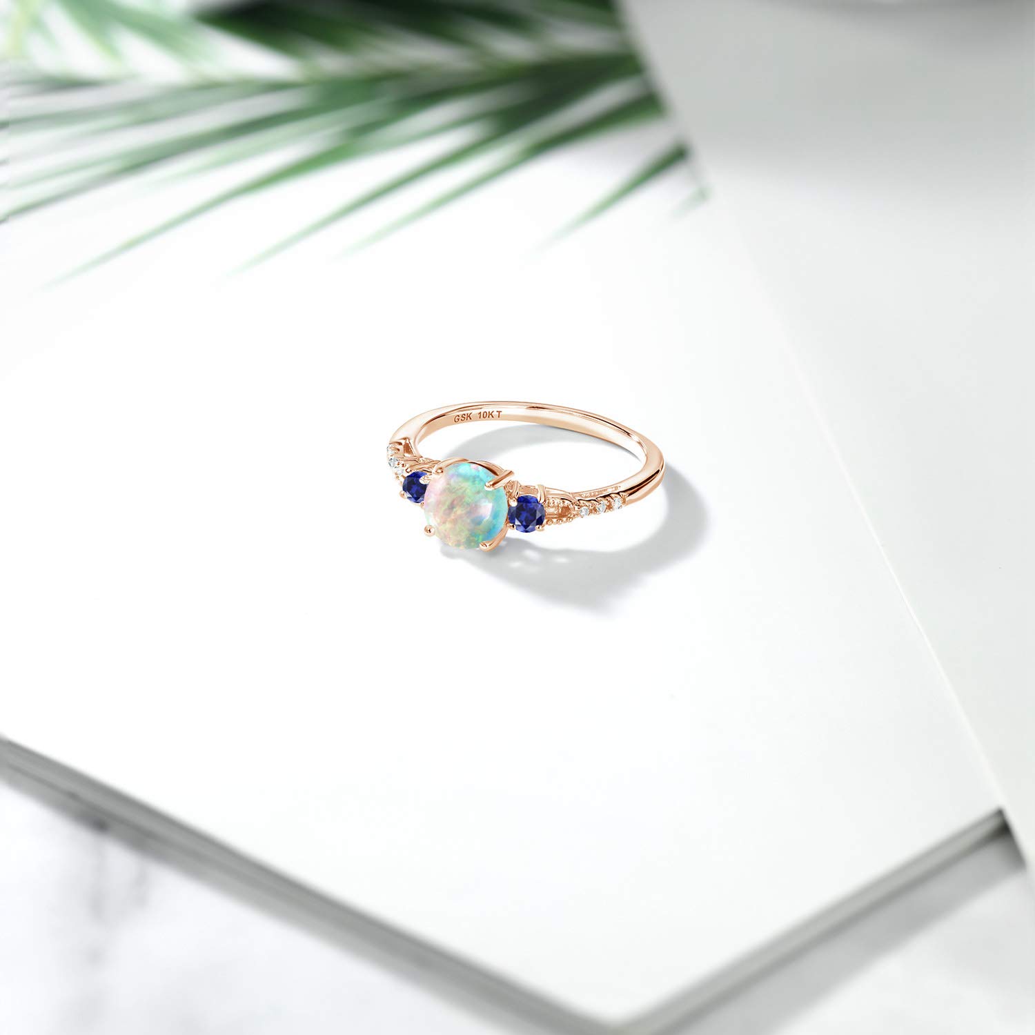 Gem Stone King 10K Rose Gold White Simulated Opal Blue Created Sapphire and White Diamond Accent 3-Stone Engagement Ring For Women (0.95 Cttw, Round Cabochon 6MM, Gemstone October Birthstone, Size 9)